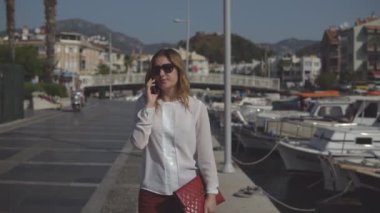 Olumlu iş kadını yürüyüş ve arka plan pier deniz telefonda konuşurken güneş gözlüğü.