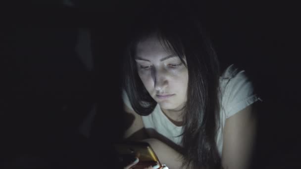 Mladá žena ve tmě v noci sedí s telefonem v sociálních sítích
