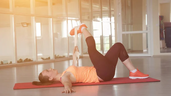 Joven hermosa mujer en ropa deportiva haciendo el calentamiento en la alfombra en el gimnasio con cinta . — Foto de Stock