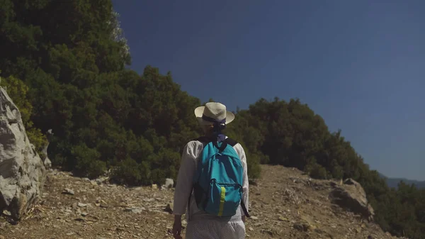 Junges Touristenmädchen mit Hut und Rucksack lächelnd auf dem Weg durch die wunderschöne Natur. — Stockfoto