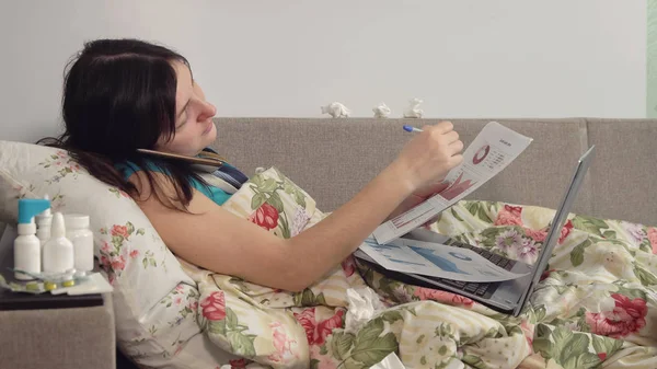Kranke Frau liegt zu Hause im Bett, telefoniert und arbeitet am Laptop — Stockfoto