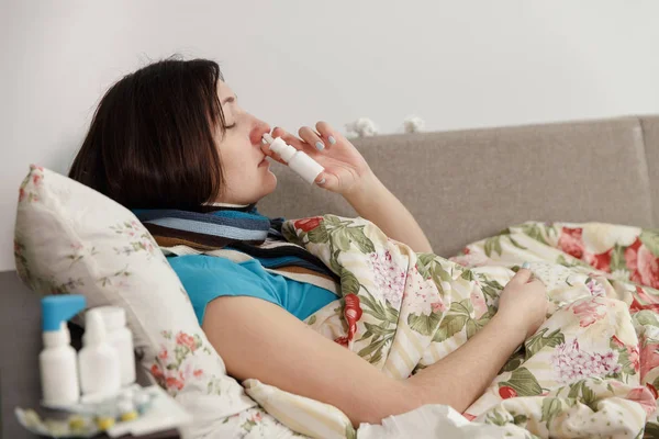 Mujer enferma acostada en la cama en casa, con spray en la nariz —  Fotos de Stock