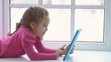 pembe elbiseli gelişmiş kız bir tablet ile cam kenarında oturan