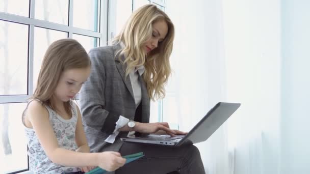 Jonge zakenvrouw zitten bij het raam met haar dochter en laptop — Stockvideo