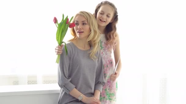 A filha deu à mãe um buquê de tulipas e um postal feito com as próprias mãos. Mãe feliz — Vídeo de Stock