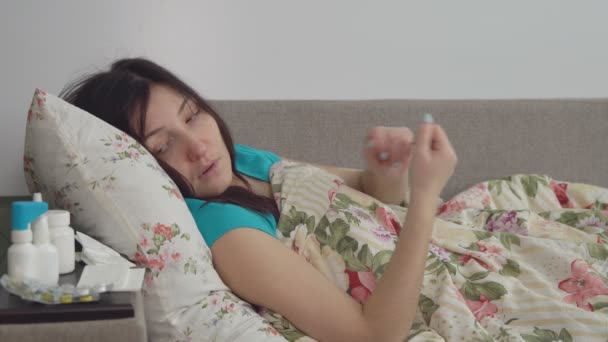Una joven con un resfriado. Se sienta en una cama en una manta — Vídeo de stock