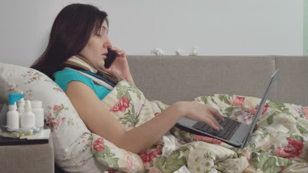 Nemocná žena ležela v posteli doma, mluvící na telefonu a práci na notebooku — Stock video