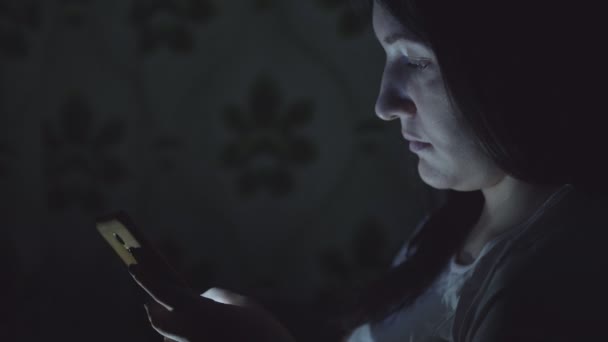 Young woman in the dark sits with a phone in social networks — Stock Video