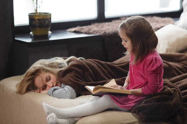 Anne uyurken kızı yatakta kitap okur