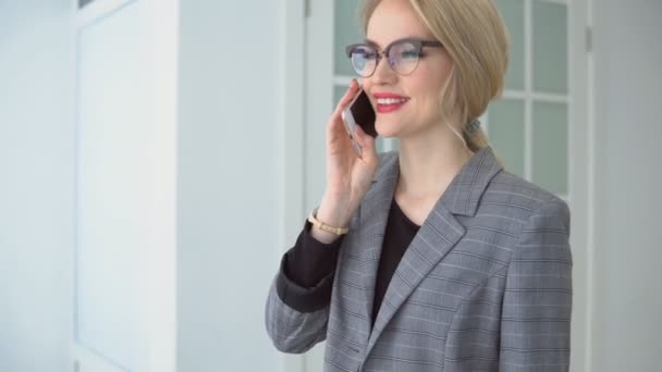 Mujer joven con una chaqueta gris hablando por teléfono sonriendo — Vídeos de Stock