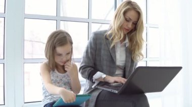 Genç iş kadını ile laptop ve küçük kızı pencerenin kenarında oturuyor