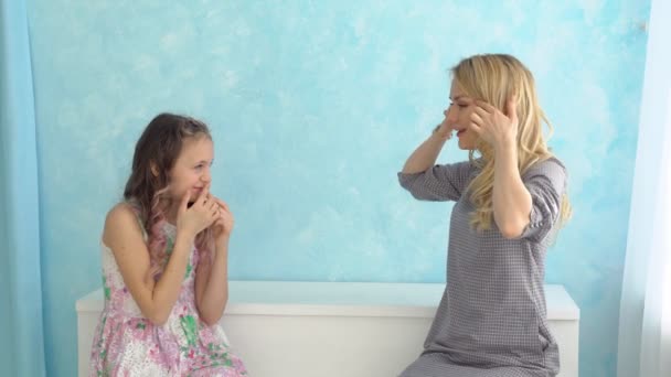 Anya és lánya egymás mellett ülnek, és vonaglik a kék falnak arcok — Stock videók