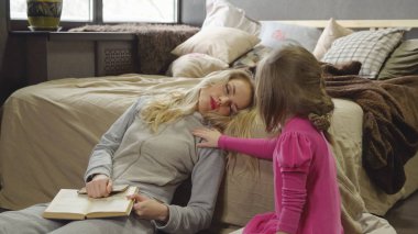 Anne ve kızı bir kitapla yatağın yanında katta oturuyor