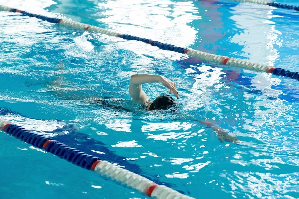 Young girl in goggles and cap swimming crawl stroke style in the blue water pool. — Stock Photo, Image