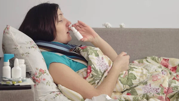 Sick woman lying in bed at home, spray in nose