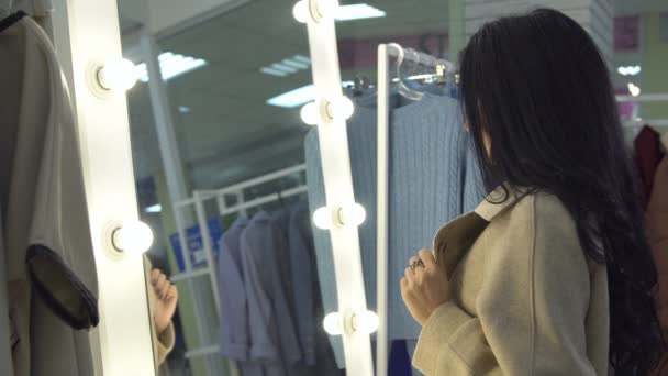 Jeune femme mesurant manteau devant un miroir dans un magasin de vêtements — Video