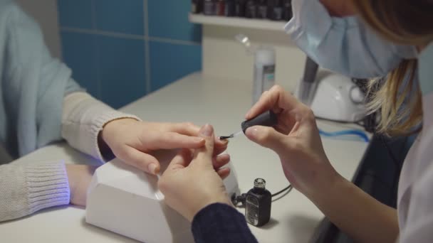 Догляд за нігтями в салоні. Майстер наносить гель-лак на цвяхи клієнта — стокове відео