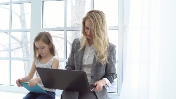 Деловая мать с ноутбуком и дочерью сидит у окна — стоковое видео