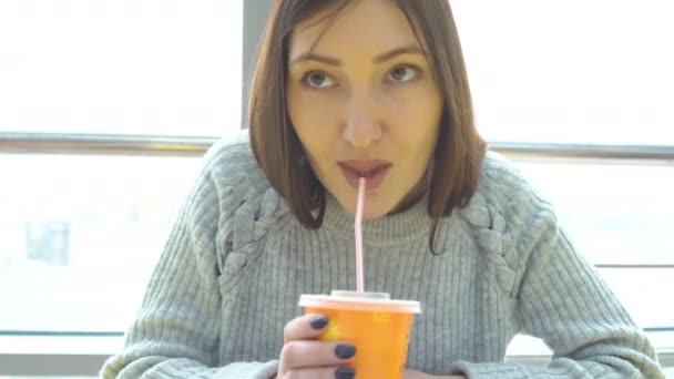 Ung kvinna dricker färskpressad juice på ett café — Stockvideo