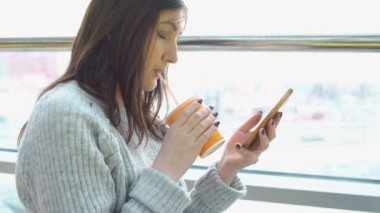 Suyu içme pencereden bir kafede bir telefon olan gri süveterli kadın