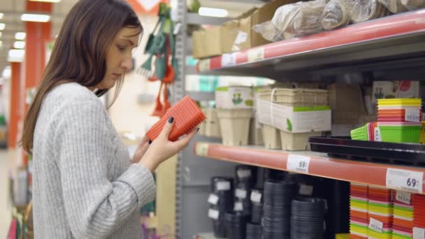 Tienda de productos para el jardín. Mujer joven elige contenedores para plántulas de flores — Vídeos de Stock