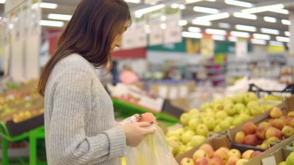 Mujer joven en el departamento de verduras de un supermercado está recogiendo manzanas — Vídeos de Stock