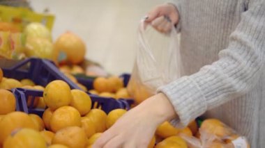 Süpermarket sebze bölümünde genç kadın bir torba mandalina çevirir
