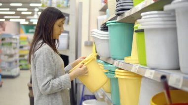 Ev için mal satışı. Genç bir kadın plastik bir kova seçiyor.