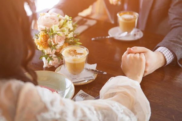 Narzeczeni w luksusowej restauracji, trzymając się za ręce i picia filiżankę kawy latte. — Zdjęcie stockowe