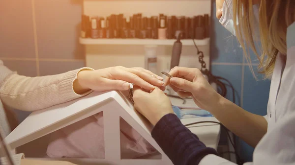 Nagel master behandelt de schubbenlaag van een jonge client met manicure pincet in een schoonheidssalon — Stockfoto