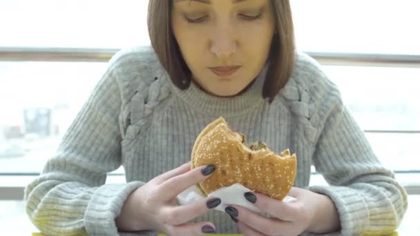 Фастфуд. Молодая женщина с аппетитом ест бургер — стоковое видео