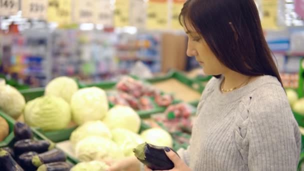 Mladá žena v departementu zeleniny supermarketu zvolí lilek — Stock video