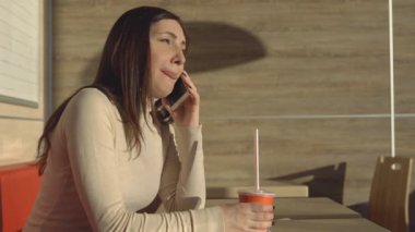 Genç esmer kadın bir kafede içecekler suyu ve telefonda konuşurken