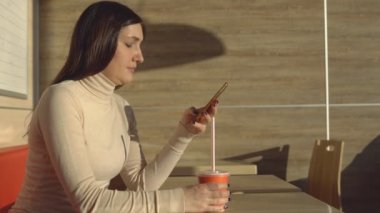 Telefon ile kafede oturan ve suyu içme genç esmer kadın