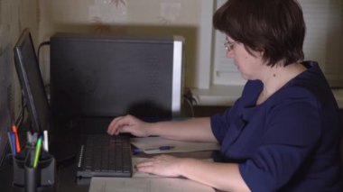 Orta yaşlı kadın gözlük bilgisayar başında oturuyor. Uzaktan çalışma