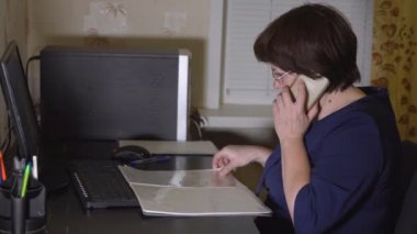 Bilgisayar başında çalışırken gözlüklü kadın telefonla konuşuyor