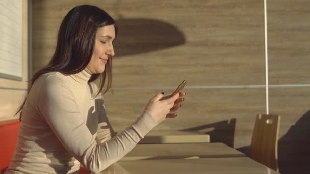 Mujer morena joven sentada en la cafetería con teléfono. comunicación virtual — Vídeos de Stock