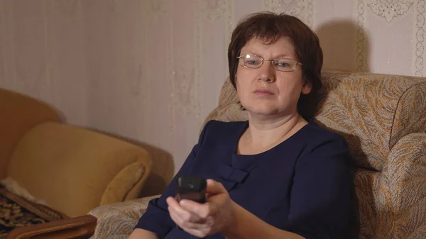 Женщина в очках переключает телеканалы с дистанционным управлением — стоковое фото