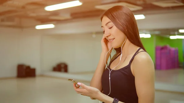 Mujer joven en uniforme deportivo con teléfono y auriculares en el gimnasio — Foto de Stock