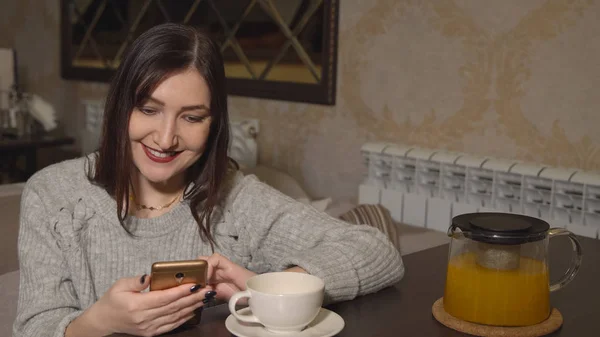 Woman in a cafe at a table drinking tea and leafing through a tape of social networks — Stock Photo, Image