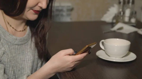 Młoda kobieta siedzi w kawiarni z telefonu i picie herbaty — Zdjęcie stockowe