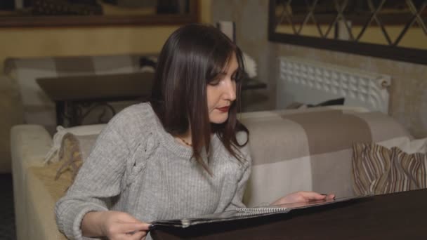 Jeune femme dans le café examine le menu — Video