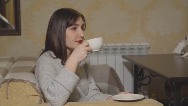 Mladá žena v kavárně pití kávy z bílého hrnečku. — Stock video