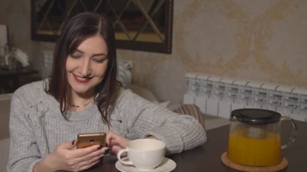 Frau in einem Café an einem Tisch trinkt Tee und blättert in sozialen Netzwerken — Stockvideo