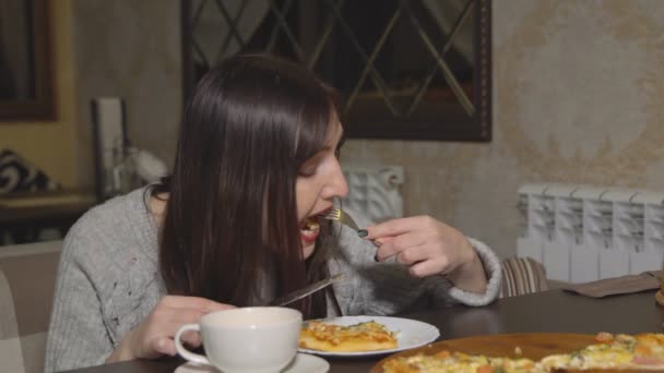 Pizzaria. Uma mulher morena comendo pizza em um café — Vídeo de Stock