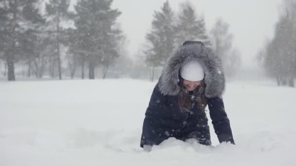 Молодая женщина падает в сугроб. Веселые прогулки в зимнем парке — стоковое видео