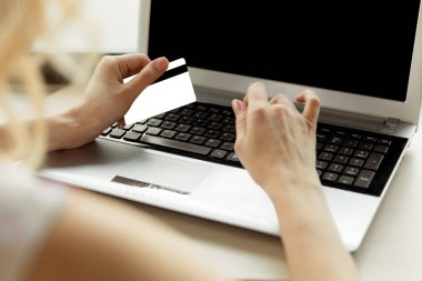 Yakın plan bir kadının elleri bir kredi kartı tutuyor ve online alışveriş için bilgisayar klavyesi kullanıyor..