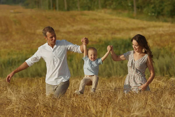 Feliz família sorrindo caminhando por um campo de trigo — Fotografia de Stock