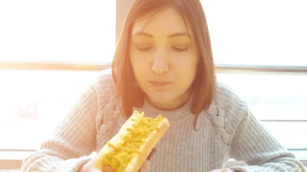 Mulher come um cachorro quente em um café fast food com apetite — Fotografia de Stock