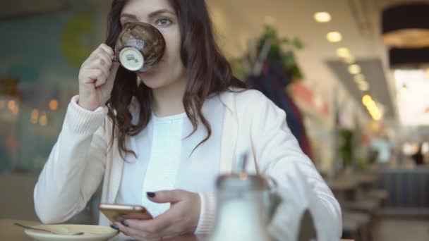 Mooie brunette vrouw met telefoon aan tafel in café — Stockvideo